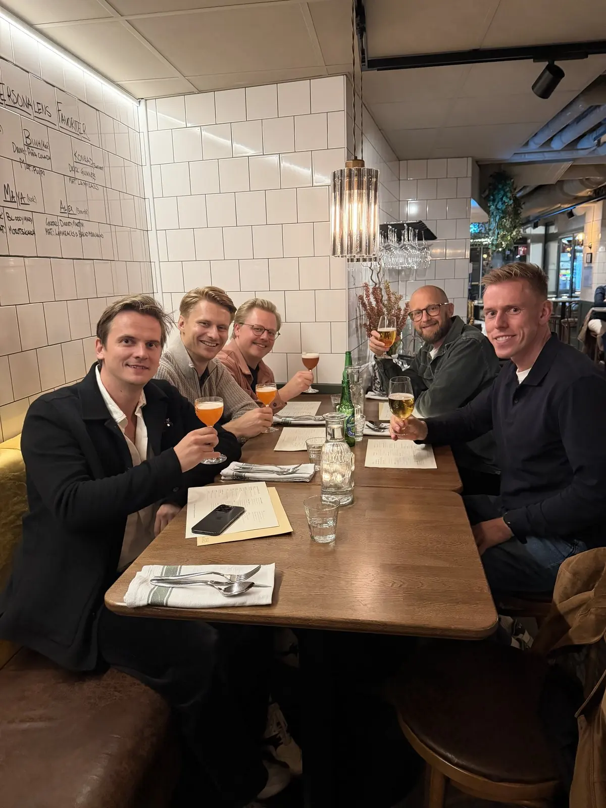 Fem kollegor höjer glasen runt ett restaurangbord.